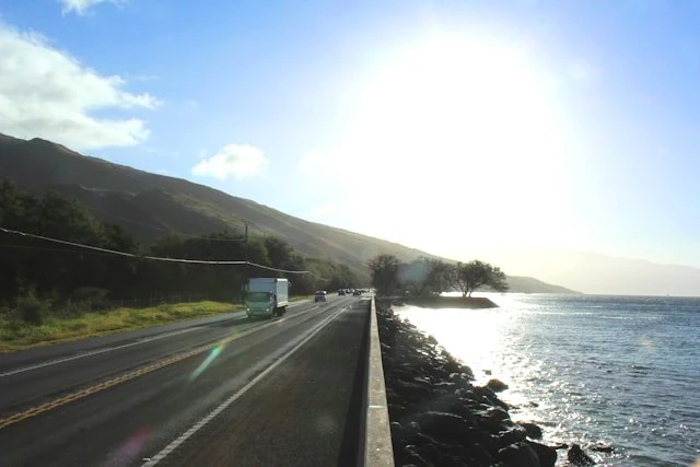 Cars driving on a coastal highway in Hawaiʻi with ocean and mountains nearby