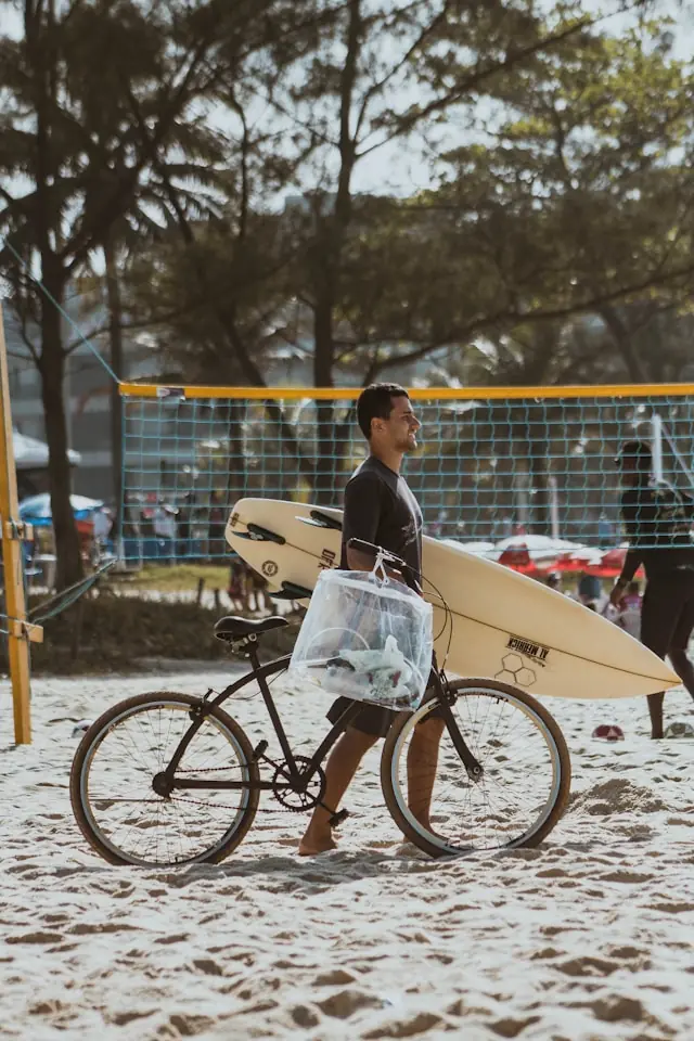 Person walking a bicycle on the beach in Honolulu, Hawaiʻi, while carrying a surfboard