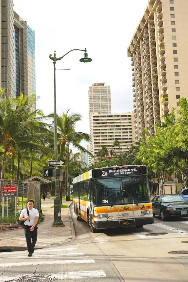City bus traveling on a street in Honolulu with buildings and pedestrians nearby
