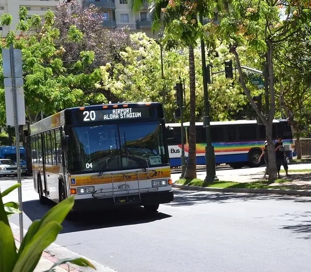 City bus driving in traffic in Honolulu with another bus in the background