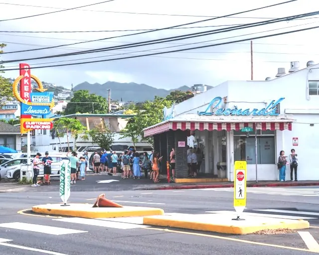 Pedestrians waiting at a crosswalk at an intersection in Honolulu with traffic nearby