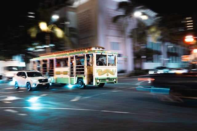 Tour trolley bus driving at night in Honolulu traffic with city lights