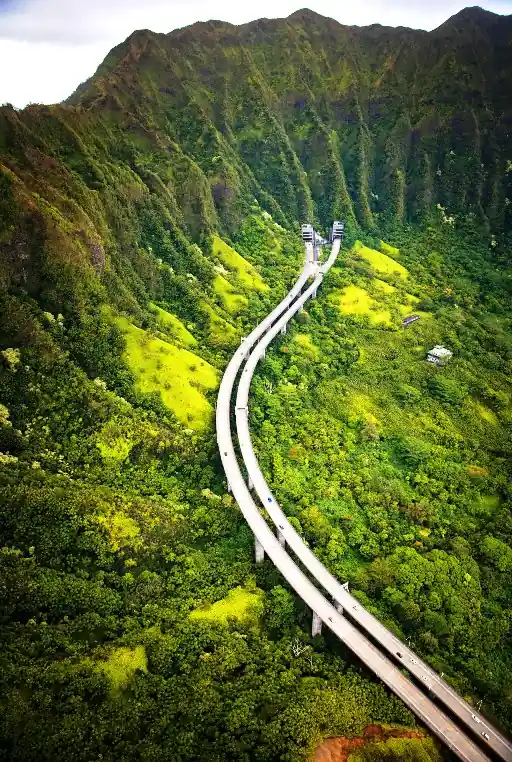 Aerial view of Interstate H-3, also known as the John A. Burns Freeway, winding through the lush green mountains of Oahu, Hawaiʻi