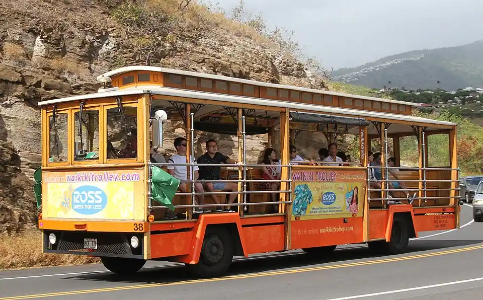Open-air trolley bus with passengers driving on a road in Waikīkī, Honolulu