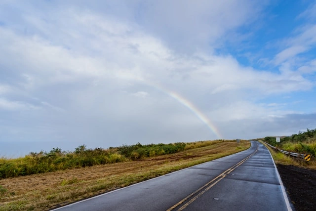 Wet Hawaiʻi road after rain with cloudy sky and rainbow