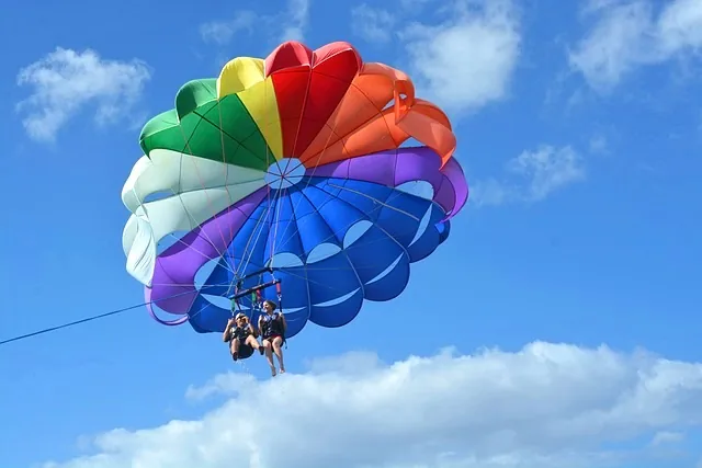 Two people secured in a parasailing harness beneath a colorful parachute during a recreational ocean excursion.