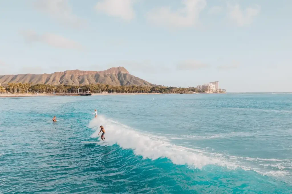 Surfer riding a breaking wave off Waikīkī with Diamond Head visible in the background on Oʻahu, Hawaiʻi.
